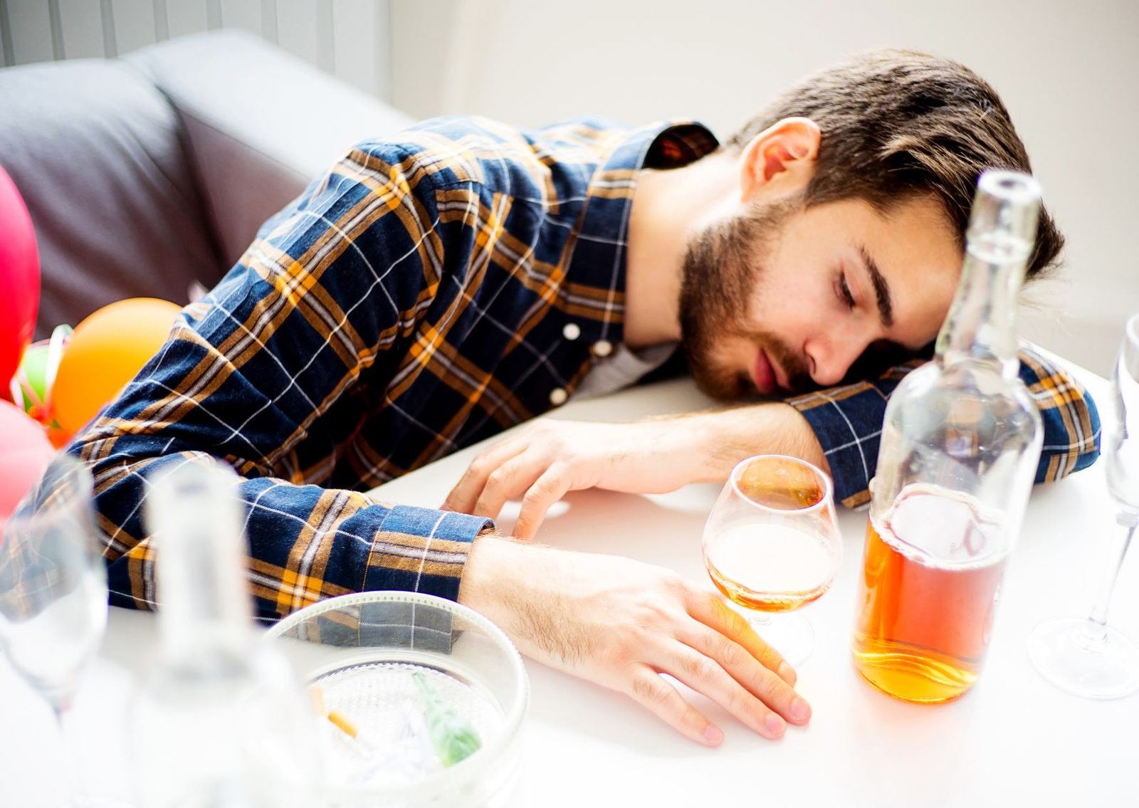 A young man asleep at a table among bottles and glasses after drinking